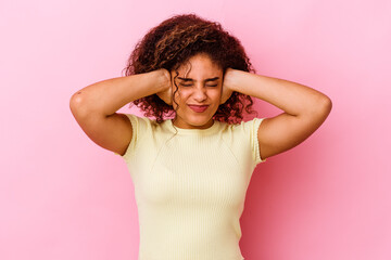 Young african american woman isolated on pink background covering ears with hands trying not to hear too loud sound.