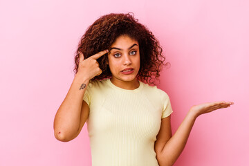 Young african american woman isolated on pink background holding and showing a product on hand.