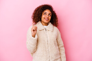 Young african american woman isolated on pink background indicates with both fore fingers up showing a blank space.