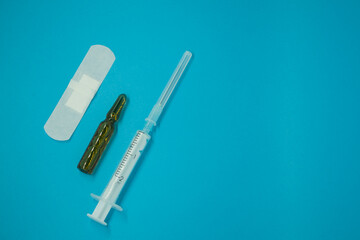 ampoule with medicine or vaccine for coronavirus, syringe and plaster. on a blue background. space for text