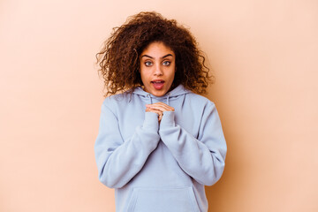 Young african american woman isolated on beige background praying for luck, amazed and opening mouth looking to front.