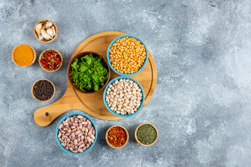 Three bowls of various beans and corns with spices on wooden board