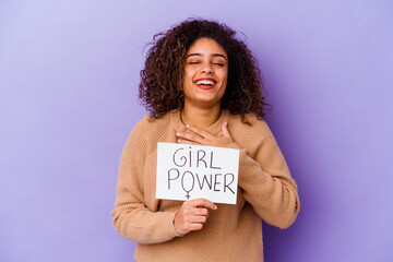 Young African American woman holding a Girl power placard isolated on purple background laughs out loudly keeping hand on chest.