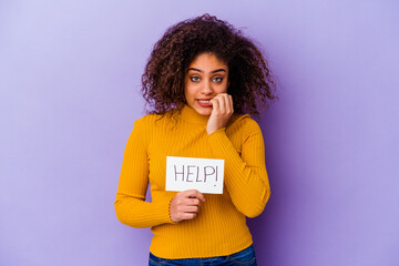 Young African American woman holding a Help placard isolated on purple background biting fingernails, nervous and very anxious.
