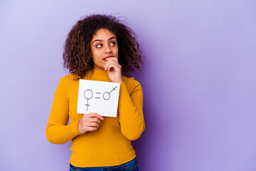 Young African American woman holding a gender equality placard isolated on purple background relaxed thinking about something looking at a copy space.