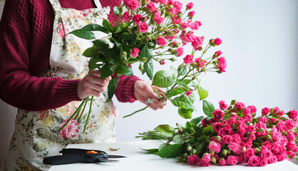 Close-up of a woman florist's hand in a flower apron making a bouquet of pink roses in a flower shop at work. The concept of the work of the florist in the store