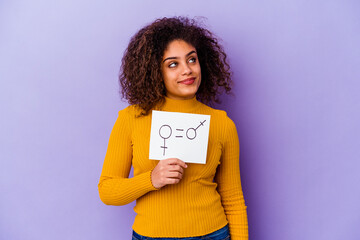 Young African American woman holding a gender equality placard isolated on purple background dreaming of achieving goals and purposes