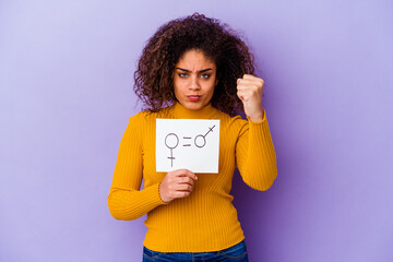 Young African American woman holding a gender equality placard isolated on purple background showing fist to camera, aggressive facial expression.