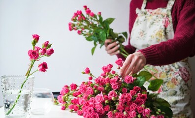 Close-up of a woman florist's hand in a flower apron making a bouquet of pink roses in a flower shop at work. The concept of the work of the florist in the store