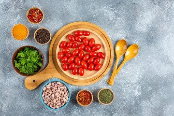 Bowl of raw beans, tomatoes and spices on marble background