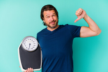 Middle age dutch man holding a scale isolated on blue background feels proud and self confident,...