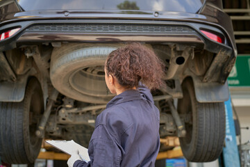 Mechanic female check chart before repair car on hydraulic lift in car garage - Powered by Adobe