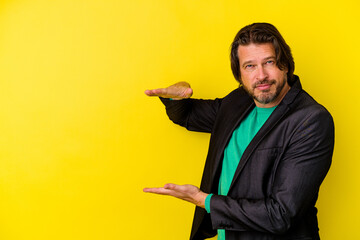 Fototapeta premium Middle age caucasian man isolated on yellow background shocked and amazed holding a copy space between hands.
