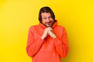 Middle age caucasian man isolated on yellow background keeps hands under chin, is looking happily aside.