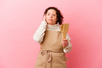 Woman with Down syndrome cooking at home isolated on pink background covering ears with hands.
