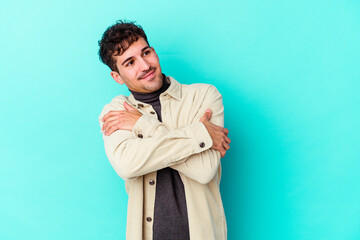Young caucasian man isolated on blue background hugs, smiling carefree and happy.