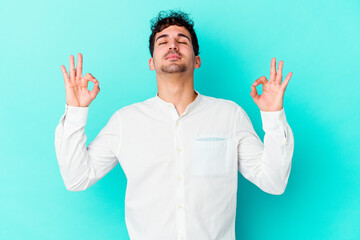 Young caucasian man isolated on blue background relaxes after hard working day, she is performing yoga.