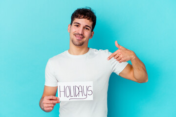 Young caucasian man holding a holidays placard isolated person pointing by hand to a shirt copy space, proud and confident