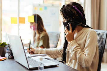 Business women wearing protective masks sitting at their desks separated by plexiglass dividers