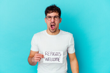 Young caucasian man holding a Refugees welcome placard isolated screaming very angry and aggressive.