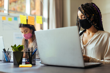 Business women wearing protective masks sitting at their desks separated by plexiglass dividers