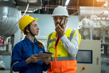 Engineer with technician working with tablet in electrical room of large industry factory.