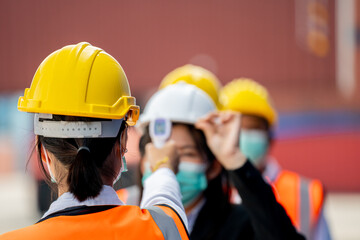 Factory woman worker in a face medical mask and safety dress used measures temperature at worker...