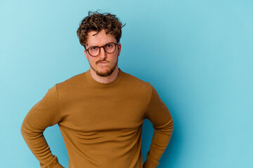 Young caucasian man wearing eyeglasses isolated on blue background blows cheeks, has tired expression. Facial expression concept.