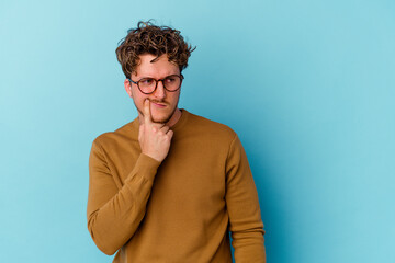Obraz na płótnie Canvas Young caucasian man wearing eyeglasses isolated on blue background contemplating, planning a strategy, thinking about the way of a business.