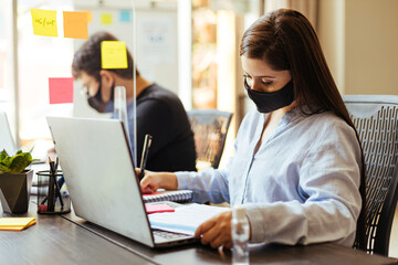 Business team wearing protective masks sitting at their desks separated by plexiglass dividers