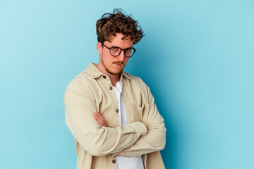 Young caucasian man wearing eyeglasses isolated on blue background frowning face in displeasure, keeps arms folded.