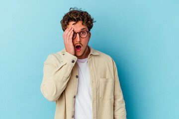 Young caucasian man wearing eyeglasses isolated on blue background having fun covering half of face with palm.