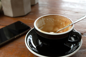 Smartphone and empty coffee cup on wooden table.