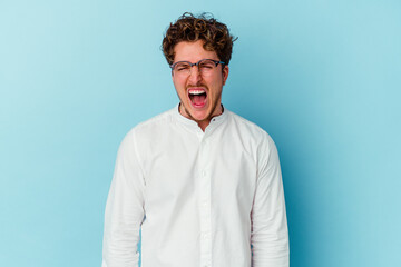 Young caucasian business man isolated on blue background screaming very angry and aggressive.