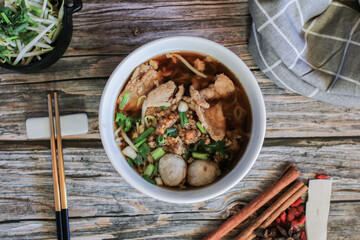 Egg noodle with pork and vegetable in five spices black soup on wooden table top view- Asian food style.
