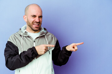 Young caucasian bald man isolated on purple background pointing with forefingers to a copy space,...