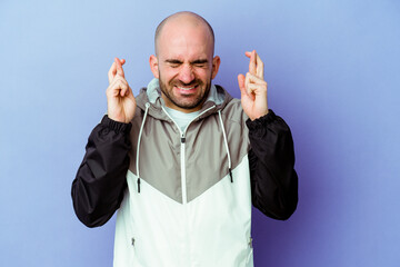 Naklejka premium Young caucasian bald man isolated on purple background crossing fingers for having luck