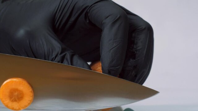 utting carrot with knife. Man hands in black gloves slice carrot