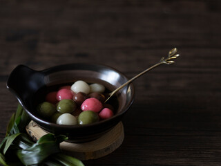 Fototapeta premium Tang Yuan (Glutinous Rice Balls) for DongZhi (Winter Solstice Festival). Colorful tang yuan side view on wooden table, dark food photography. Rice Balls close up, still life photography