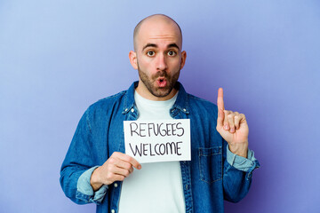 Young caucasian bald man holding a Refugees welcome placard isolated on blue background having some...