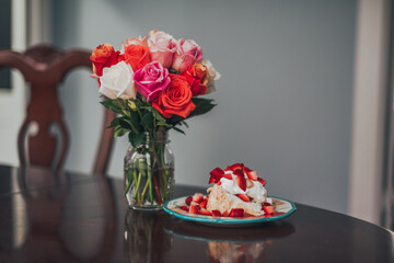 Strawberry Shortcake with strawberries, whipped cream, and angel food cake next to a vase of roses