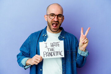 Young caucasian bald man holding a I hate the pandemic placard isolated on blue background joyful and carefree showing a peace symbol with fingers.