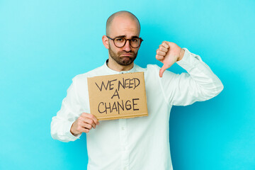 Young caucasian bald man holding a We need a change placard isolated on purple background showing a...