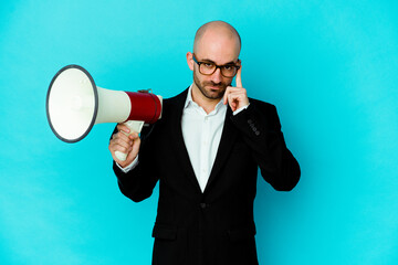 Young business bald man holding a megaphone isolated pointing temple with finger, thinking, focused on a task.