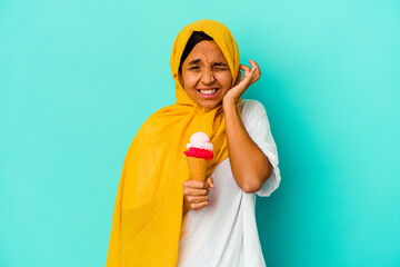 Young muslim woman eating an ice cream isolated on blue background covering ears with hands.