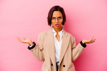 Young business mixed race woman isolated on pink background doubting and shrugging shoulders in...