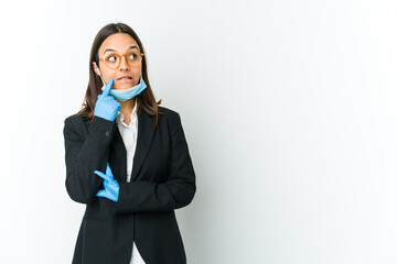 Young business latin woman wearing a mask to protect from covid isolated on white background relaxed thinking about something looking at a copy space.