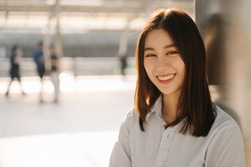 Portrait of beautiful Asian young entrepreneur standing leaning against pillar outside office while smiling and looking at camera