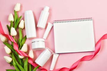 Valentines Day and Womens Day, mother's day concept. Empty white tubes and bottles with white tulips and notebook on a pink background.  Flat lay, copy space.