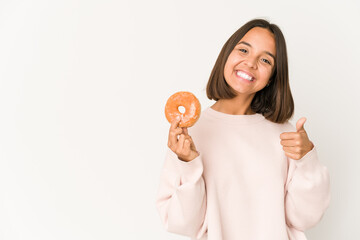 Young hispanic woman eating a doughnut smiling and raising thumb up